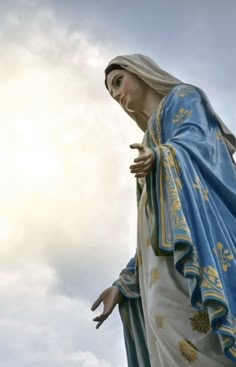 a statue of the virgin mary holding her hands out in front of a cloudy sky