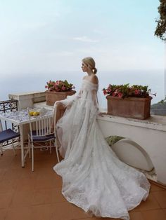 a woman in a wedding dress is sitting on a balcony overlooking the ocean and flowers