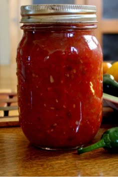 a jar filled with red sauce sitting on top of a wooden table next to vegetables