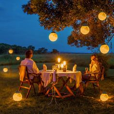 two people sitting at a table with candles in front of them, surrounded by paper lanterns