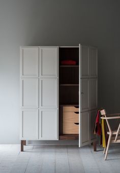 a white cabinet with drawers and clothes hanging on the door, next to a chair