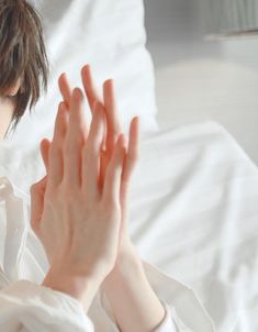 a woman in white shirt holding her hands up to the side while sitting on a bed