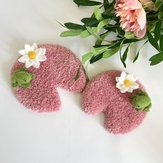 two pink teddy bears with white flowers on them sitting next to some green leaves and flowers