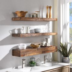 two wooden shelves with dishes and cups on them in front of a window next to a sink