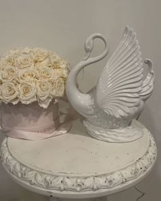 two white swan shaped vases sitting on top of a table with roses in them