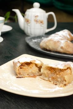 two plates with pastries on them sitting on a table next to cups and saucers