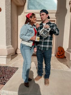 a man standing next to a woman in front of a house with pumpkins on the ground