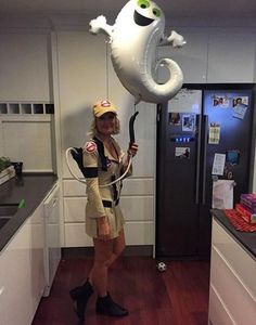 a woman is holding an inflatable balloon while standing next to a refrigerator and cabinets