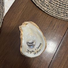 an oyster shell with a wedding ring on it sitting on a wooden floor next to a rug