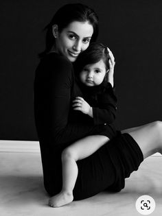 a woman sitting on the floor holding a small child in her lap and posing for a black and white photo