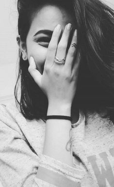 black and white photograph of a woman covering her face with her hands while looking at the camera