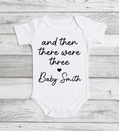 a white onesuit with black lettering that says and then there were three baby smith