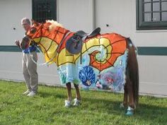 a man standing next to a brown horse wearing a colorful blanket