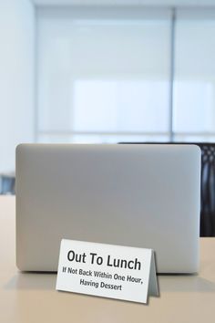 a laptop computer sitting on top of a desk next to a sign that says out to lunch if not back within one hour, having dessert