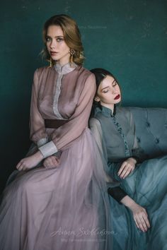 two women are sitting on a couch with their eyes closed and one is wearing a gray dress