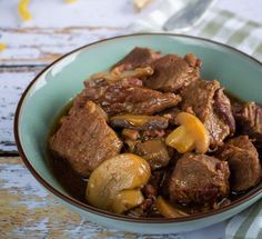 a bowl filled with meat and mushrooms on top of a tablecloth next to a fork