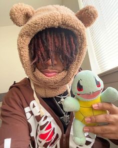 a person with dreadlocks holding a stuffed animal and wearing a hoodie over their face