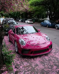 a red sports car parked on the side of a road with pink flowers all over it