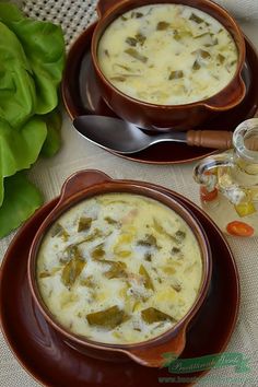 two brown bowls filled with soup on top of a table next to green leaves and spoons