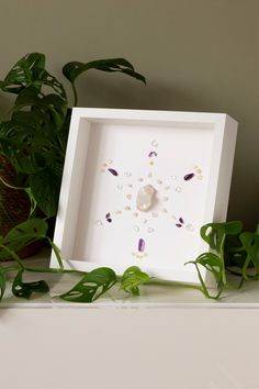 a white clock sitting on top of a table next to a potted green plant