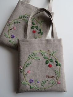 two bags with embroidered designs on them sitting next to each other, one has a strawberries and the other has flowers