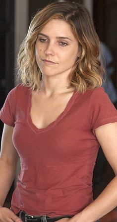 a woman standing with her hands on her hips and looking at the camera while wearing a red shirt