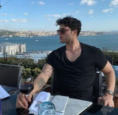 a man sitting at a table with a glass of wine in front of him and looking out over the water