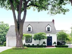 a white house with black shutters and trees in the front yard on a sunny day