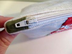 a hand holding a zipper on top of a white bag