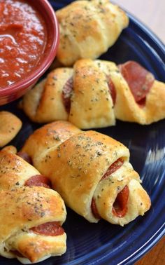 several pigs in a blanket on a blue plate with a small bowl of tomato sauce