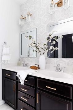 a white and black bathroom with two sinks, mirrors and vases on the counter