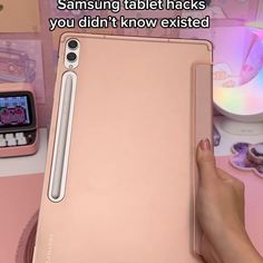 someone is holding an ipad in their hand and touching it with the other hand, next to a pink table