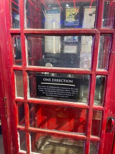 a red phone booth with one direction sign on it's glass door and another in the background