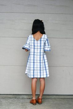 a woman standing in front of a wall with her back to the camera, wearing a blue and white plaid dress