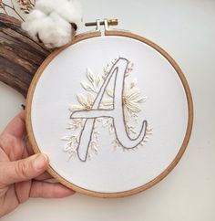 a hand embroidered monogram on a white fabric with flowers and leaves in the hoop