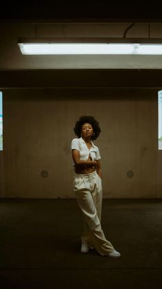 a woman standing in an empty room with her arms crossed and looking off to the side