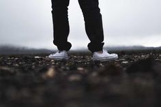 a person standing in the middle of a field with their legs crossed and shoes on