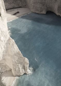 the water is blue and clear at the bottom of the cliff, with white cliffs in the background