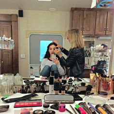 two women sitting at a vanity in front of a mirror with makeup products on it