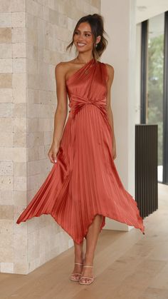 a woman standing in front of a wall wearing an orange dress