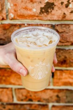 someone holding up a starbucks drink in front of a brick wall