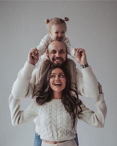 a man and woman holding a child on their shoulders while they both look at the camera