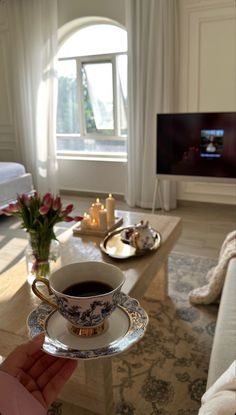 a cup of coffee on a saucer in front of a living room with candles