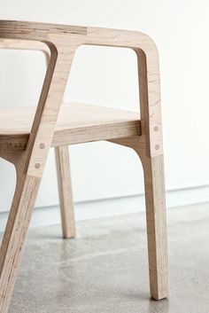 a wooden chair sitting on top of a cement floor next to a white wall,