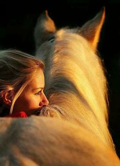 a woman with long blonde hair standing next to a white horse in the sun light