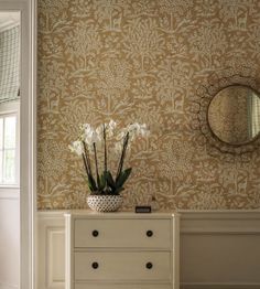 a white dresser sitting in front of a mirror next to a wall with flowers on it