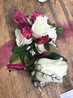 two white roses with pink ribbons on a wooden table next to a piece of paper