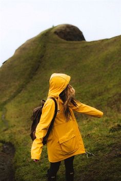 a woman in a yellow raincoat is walking up a hill with her back to the camera