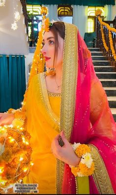 a woman dressed in yellow and pink is standing on the stairs with flowers around her neck