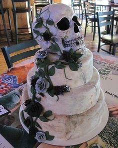 a three tiered cake decorated with flowers and a skull on the top is sitting on a table